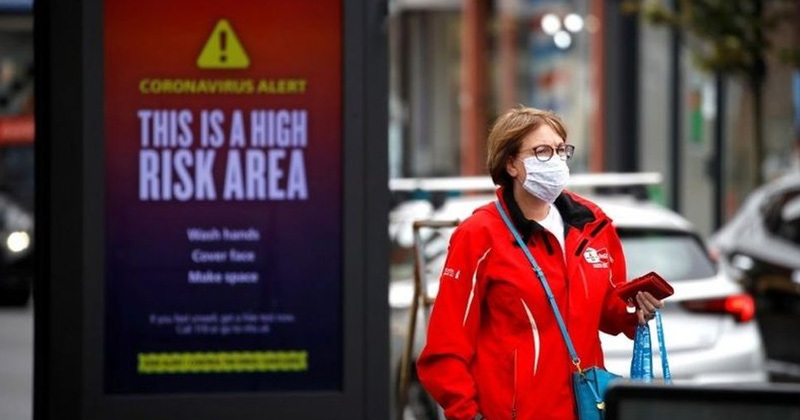 A woman walking past a billboard about covid 19 alert | Coronavirus New Strains Wreaking Havoc In Europe